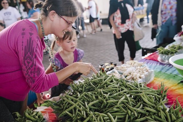 Mother and daughter at the farmers market, looking at a bountiful harvest of green beans